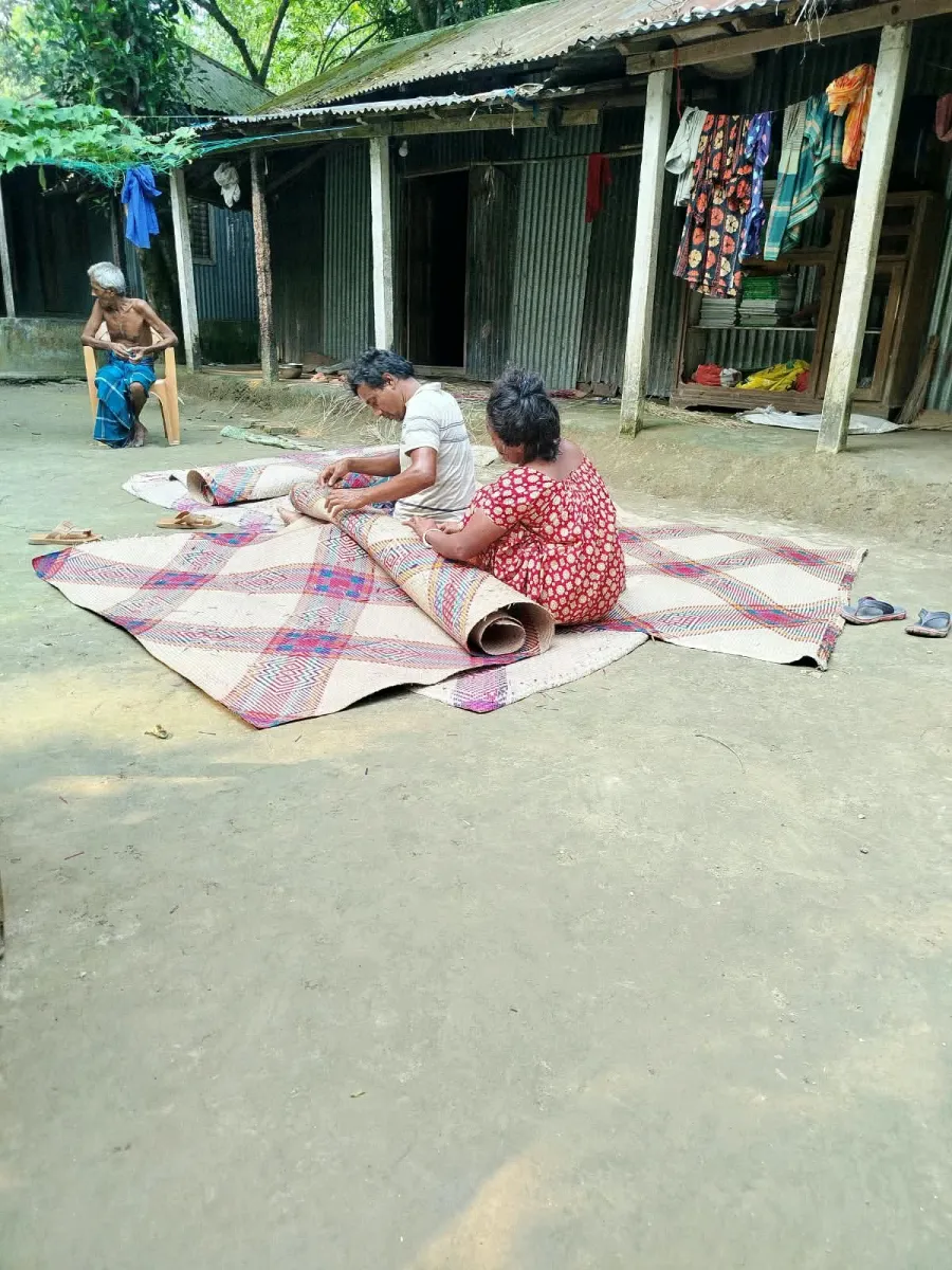 Two makers rolling out a finished Shitol Pati mat in a courtyard at Patrail Char