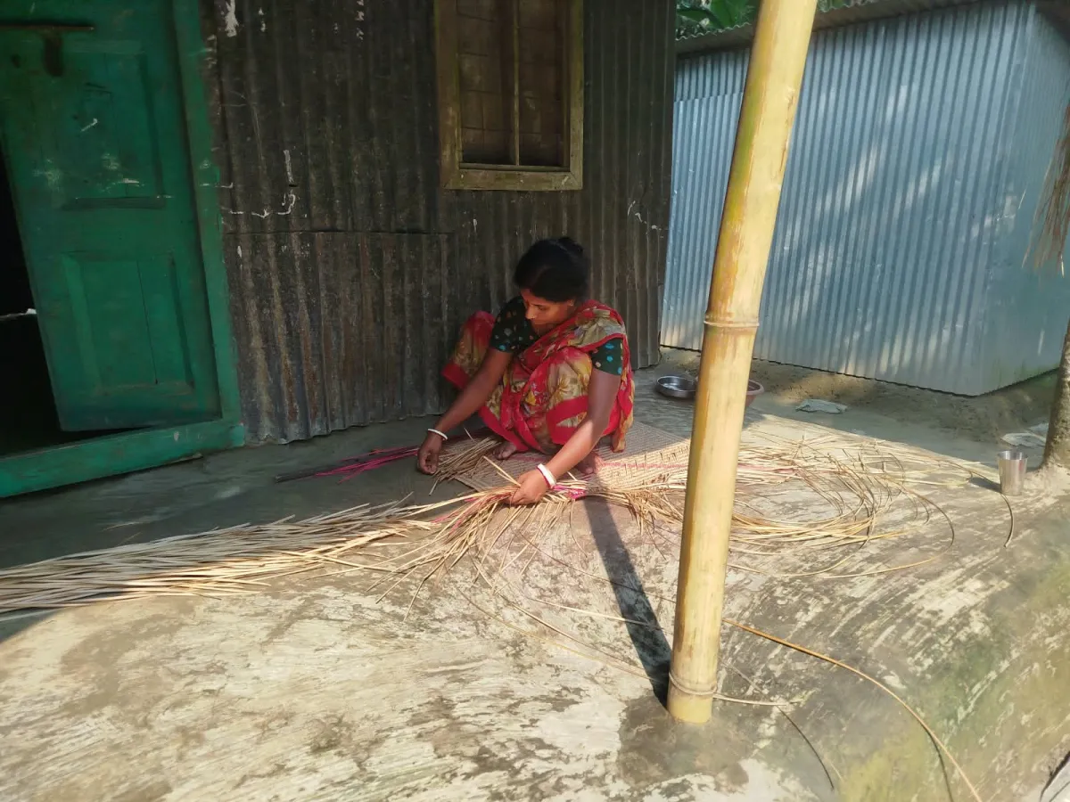 A maker weaving a Shitol Pati mat on the doorstep of her home at Patrail Char