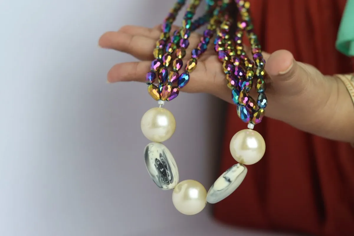 A hand holding up a necklace of shimmering beads and large white pearls