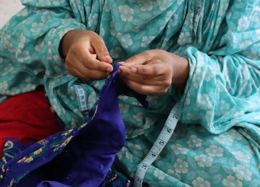 Hands working a needle through deep blue fabric, a measuring tape over the knee