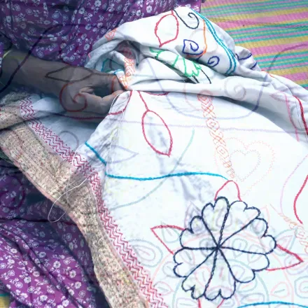 Close-up of hands running coloured thread through a Nakshi Kantha floral motif