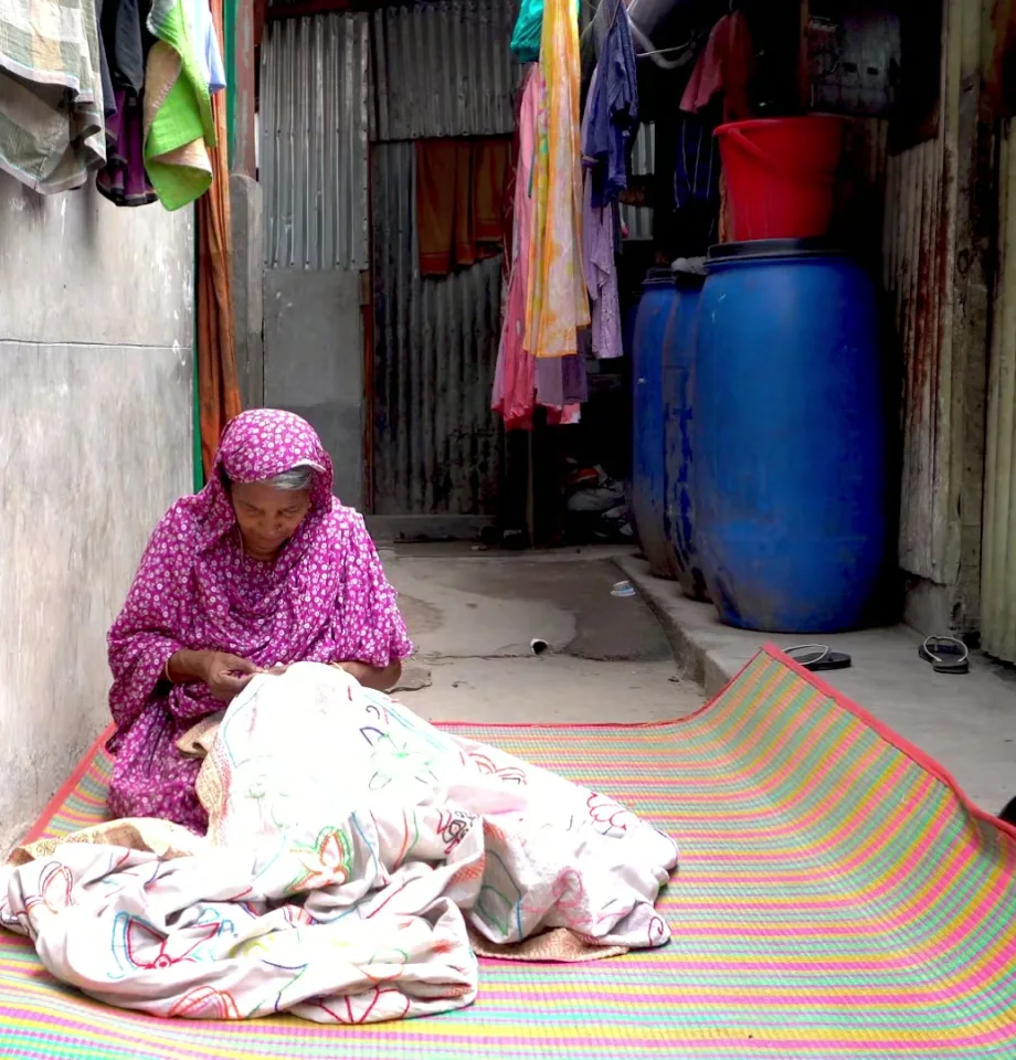 An artisan seated in a courtyard, hand-stitching a Nakshi Kantha quilt