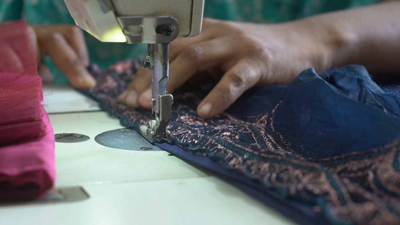 Hands guiding embroidered fabric under a sewing machine needle