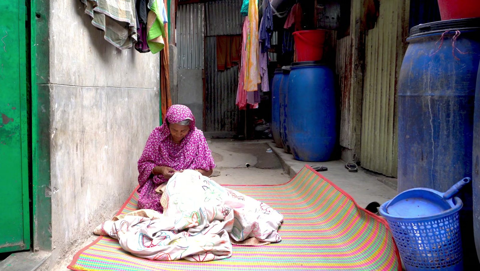 An artisan embroidering a Nakshi Kantha quilt beside a window